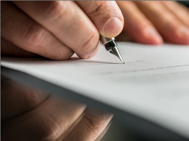 A person signing a contract on top of a reflective table